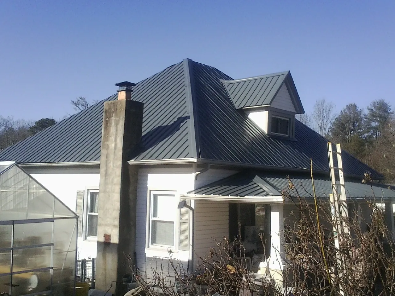 Dark blue standing seam metal roof on a white farmhouse with dormer — Slate & Tile Roof Repair by Roofing Brothers in Saint Louis