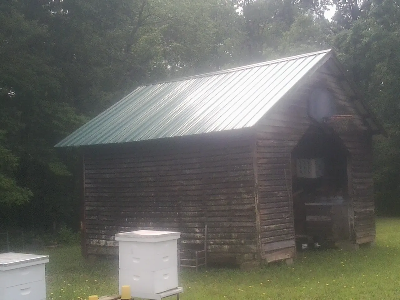 Green metal roof on a weathered barn beside stacked beehives in Saint Louis