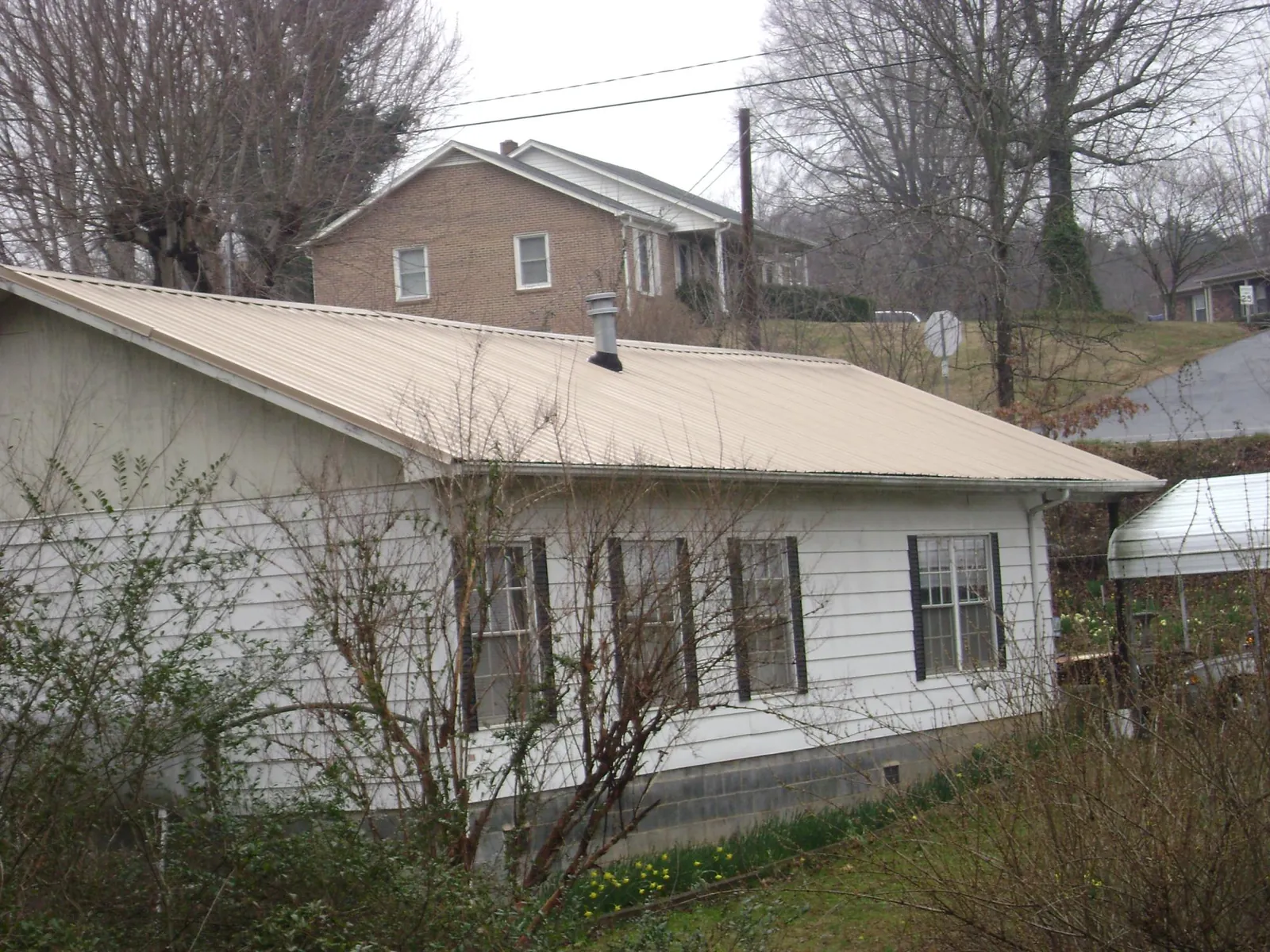 Tan metal roof on a white sided house set into a hillside — Commercial Roofing by Roofing Brothers in Saint Louis